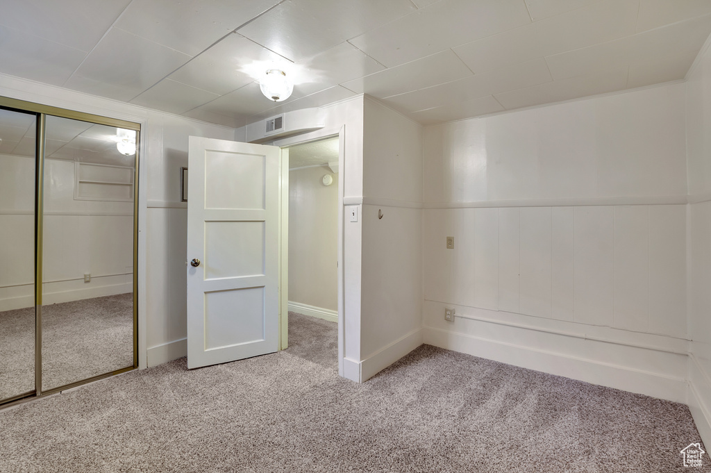 Unfurnished bedroom with carpet floors, visible vents, a wainscoted wall, and a closet