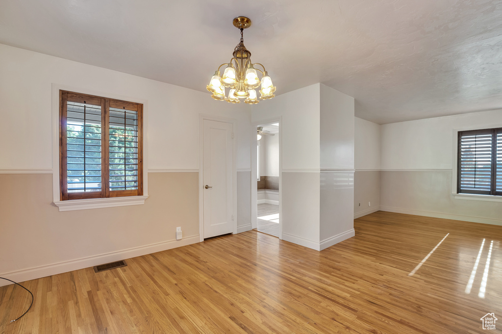 Empty room with a chandelier, baseboards, visible vents, and light wood finished floors