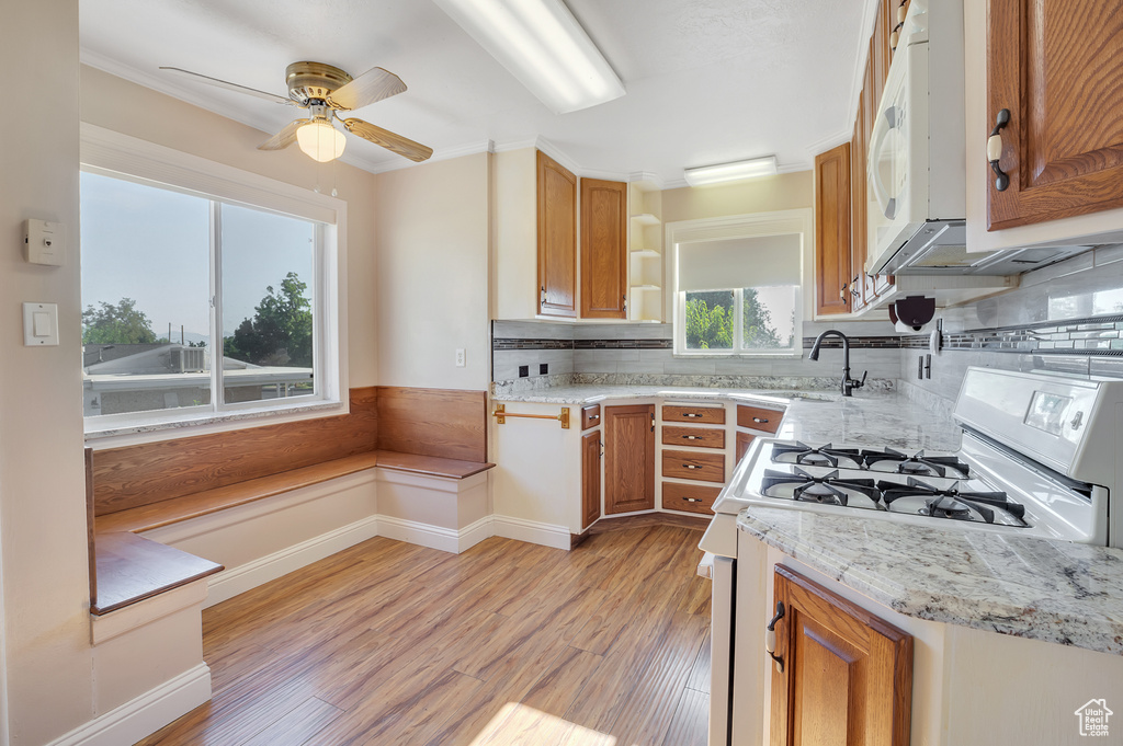 Kitchen featuring a sink, white appliances, brown cabinetry, a ceiling fan, and light wood-type flooring