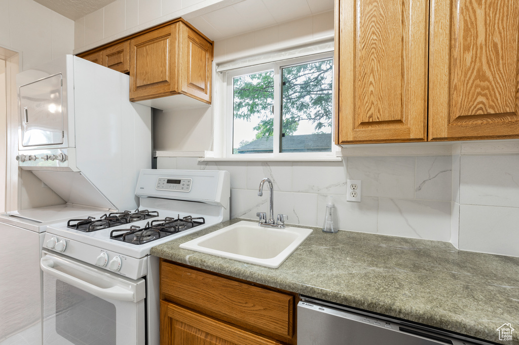 Kitchen featuring brown cabinets, a sink, dishwasher, decorative backsplash, and white range with gas stovetop