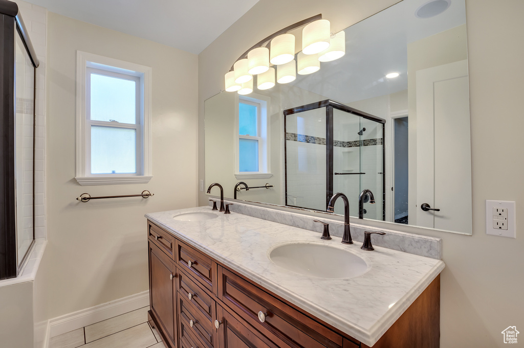 Full bathroom with baseboards, a sink, double vanity, and tiled shower