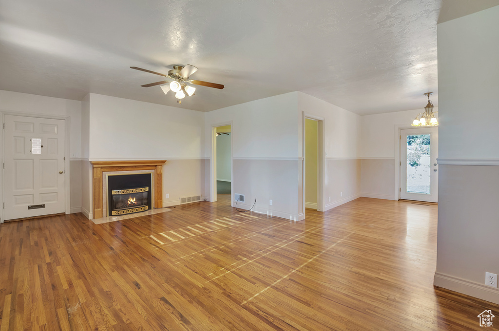 Unfurnished living room with visible vents, light wood-style floors, baseboards, a fireplace with flush hearth, and ceiling fan with notable chandelier