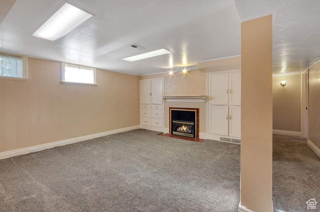 Below grade area featuring a fireplace with flush hearth, baseboards, carpet flooring, and visible vents