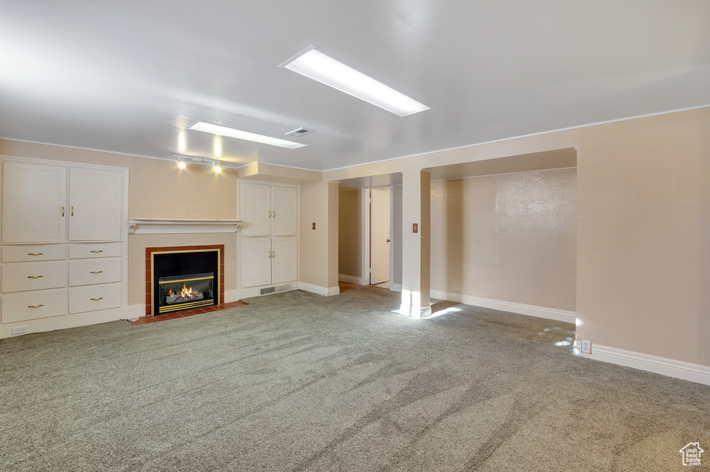 Unfurnished living room featuring carpet floors, baseboards, a tile fireplace, and visible vents