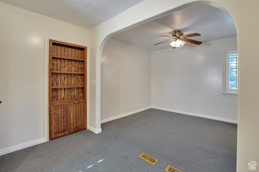 Spare room with a ceiling fan, a textured ceiling, arched walkways, baseboards, and dark carpet