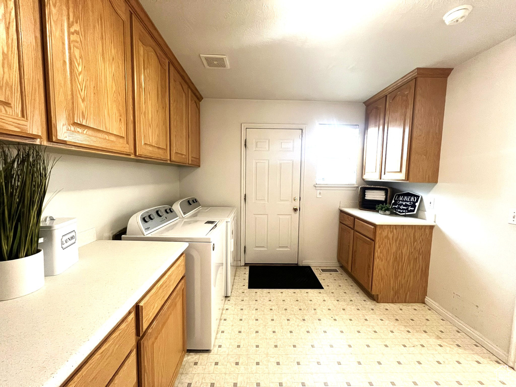 Laundry area with light floors, washing machine and dryer, baseboards, visible vents, and cabinet space