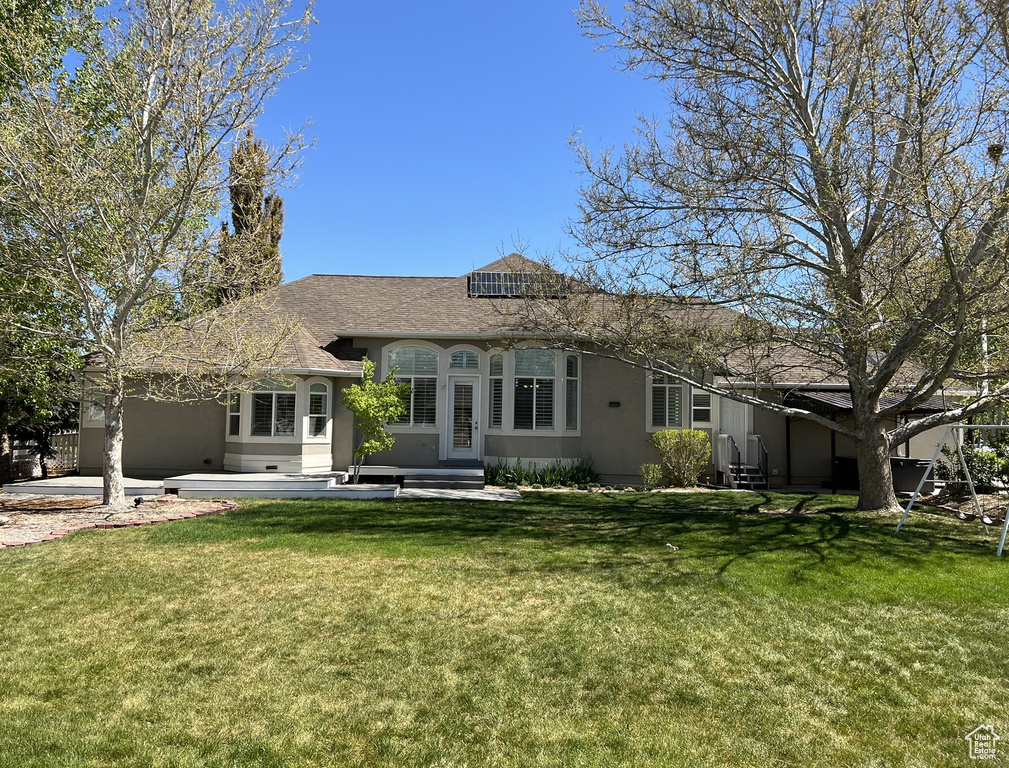 Back of house with roof mounted solar panels, roof with shingles, stucco siding, and a yard
