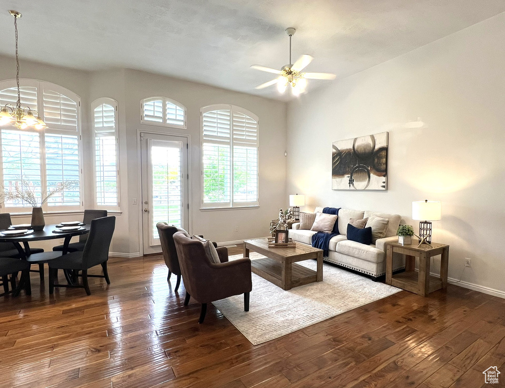 Living room with ceiling fan with notable chandelier, baseboards, and dark wood finished floors