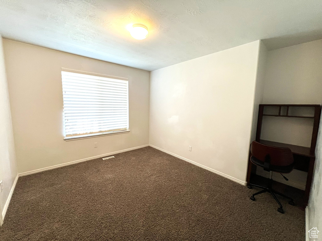 Spare room with dark colored carpet, a textured ceiling, baseboards, and visible vents