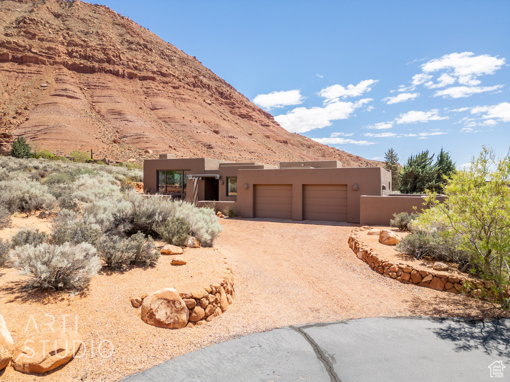 View of front of property featuring a mountain view, stucco siding, an attached garage, and dirt driveway