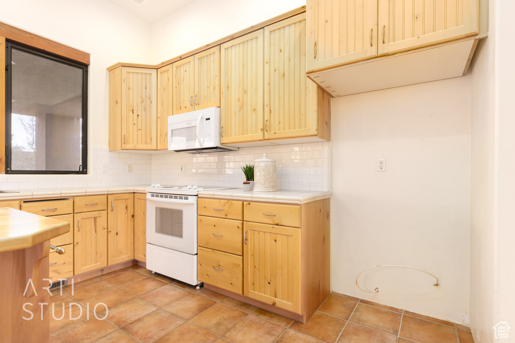 Kitchen with light brown cabinets, decorative backsplash, tile counters, and white appliances