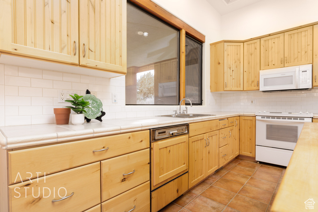 Kitchen featuring a sink, backsplash, light brown cabinets, and white appliances