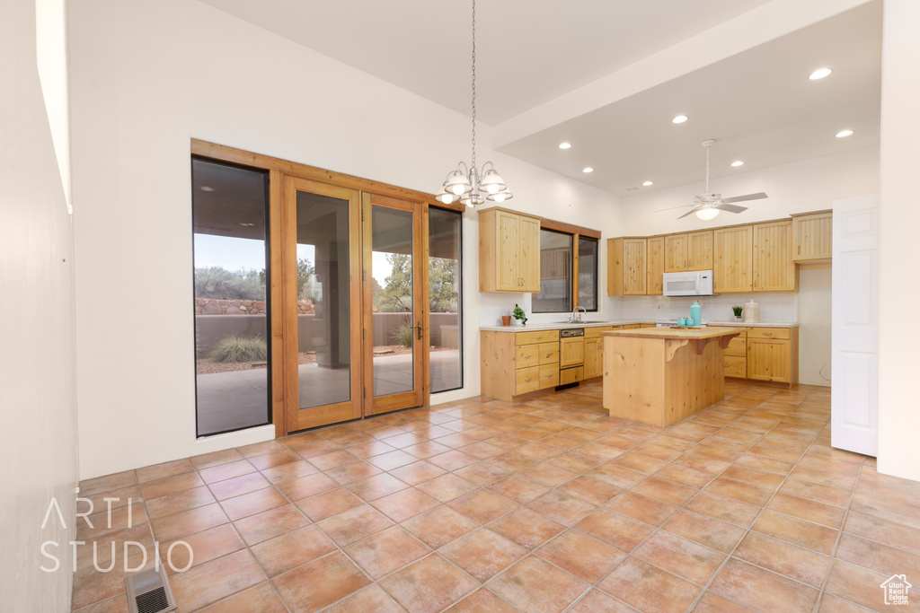 Kitchen featuring light countertops, light brown cabinets, white microwave, and a kitchen island