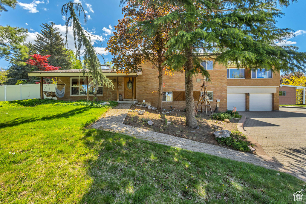 View of front of property with fence, an attached garage, a front lawn, brick siding, and decorative driveway