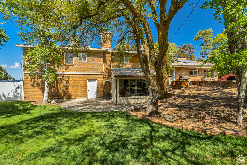 Back of house featuring a chimney, a lawn, brick siding, roof mounted solar panels, and a patio