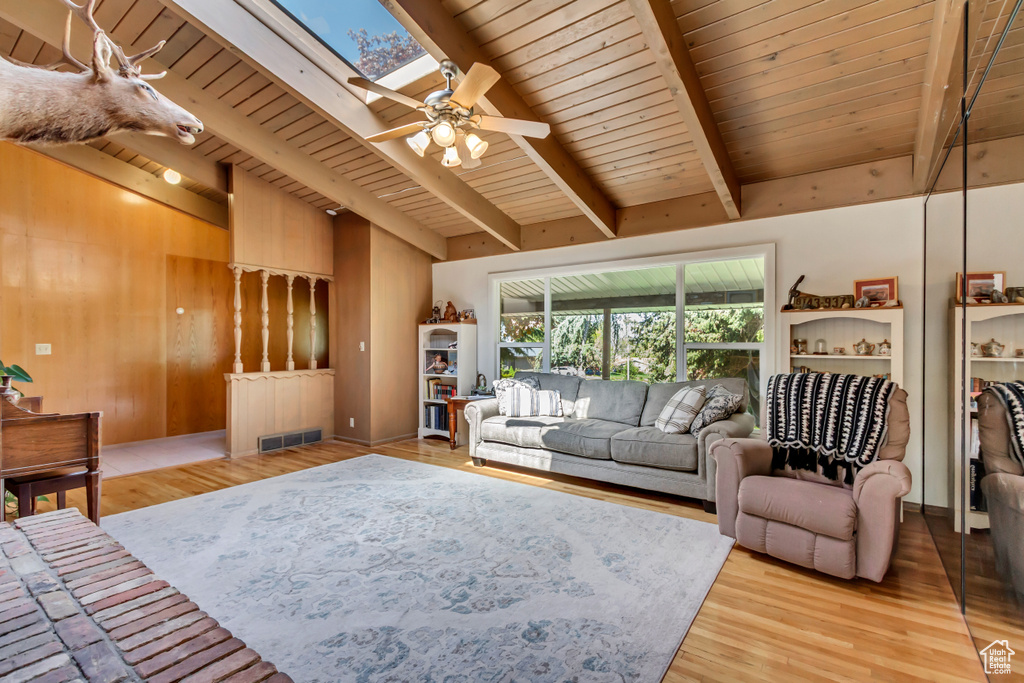 Living room with vaulted ceiling with skylight, a ceiling fan, light wood-type flooring, visible vents, and wood ceiling