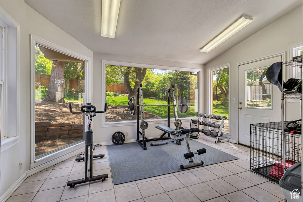 Workout area featuring baseboards, plenty of natural light, light tile patterned floors, and lofted ceiling