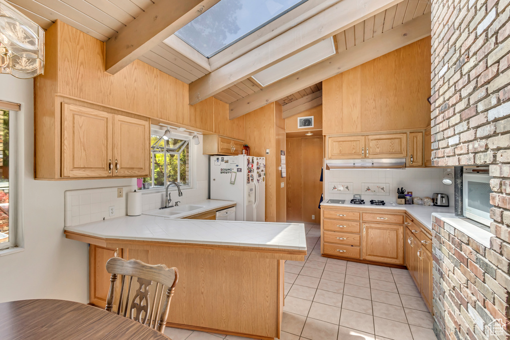 Kitchen featuring light tile patterned flooring, white appliances, vaulted ceiling with skylight, tasteful backsplash, and a sink