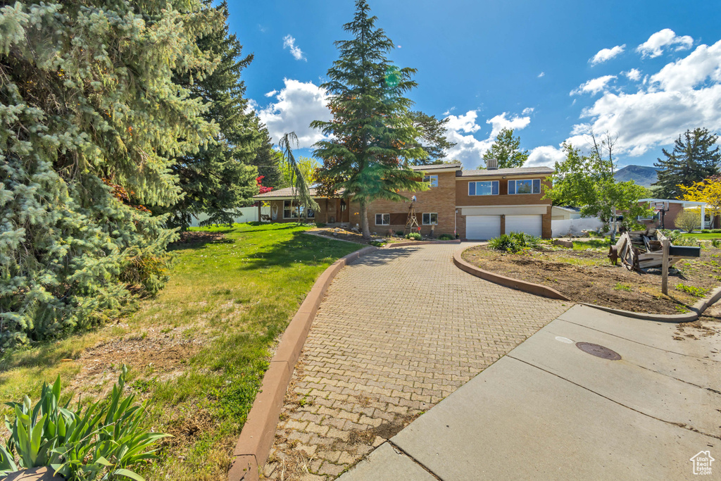 View of front of home with an attached garage, a front lawn, and decorative driveway