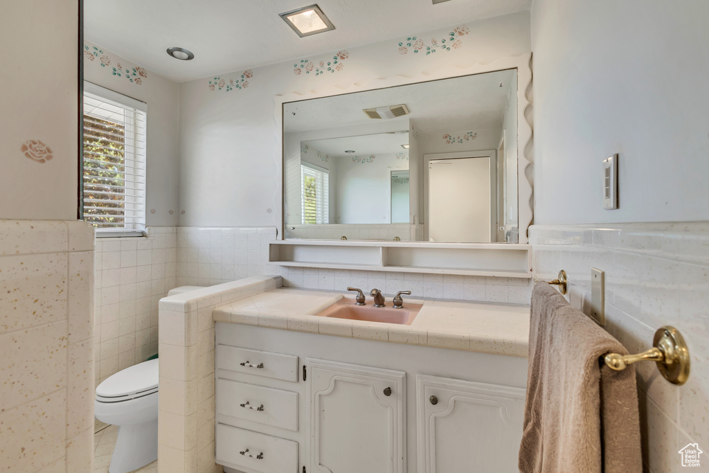 Bathroom featuring vanity, visible vents, wainscoting, toilet, and tile walls