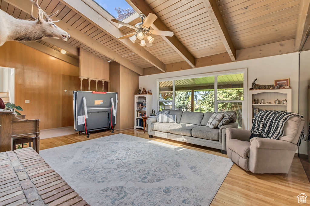 Living room with wood ceiling, ceiling fan, wood walls, light wood finished floors, and lofted ceiling with skylight
