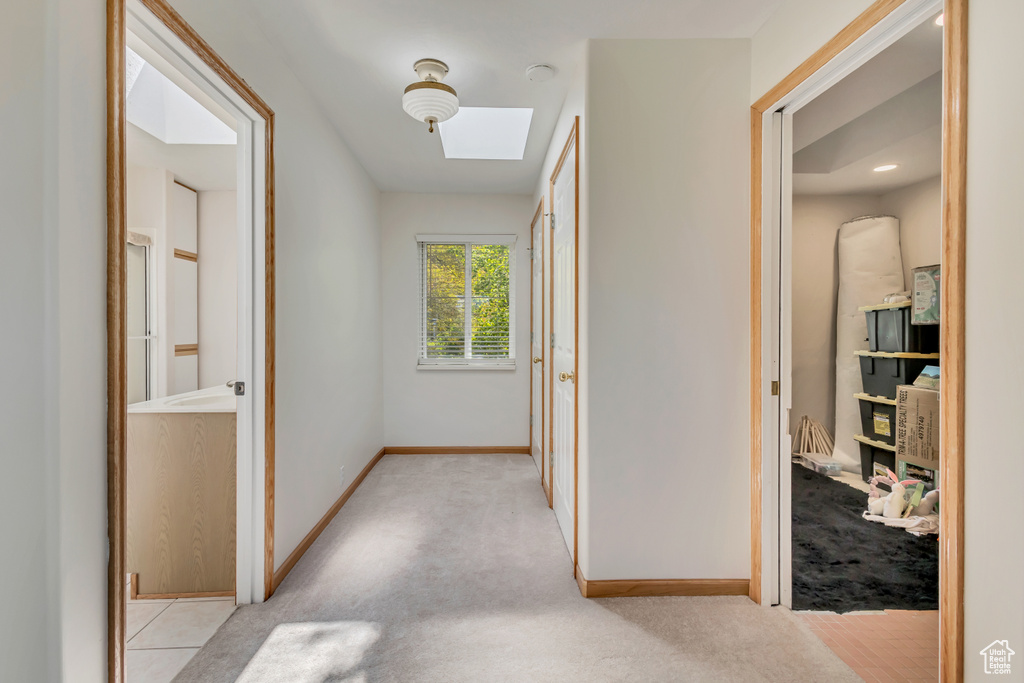 Hallway with a skylight, baseboards, and light colored carpet
