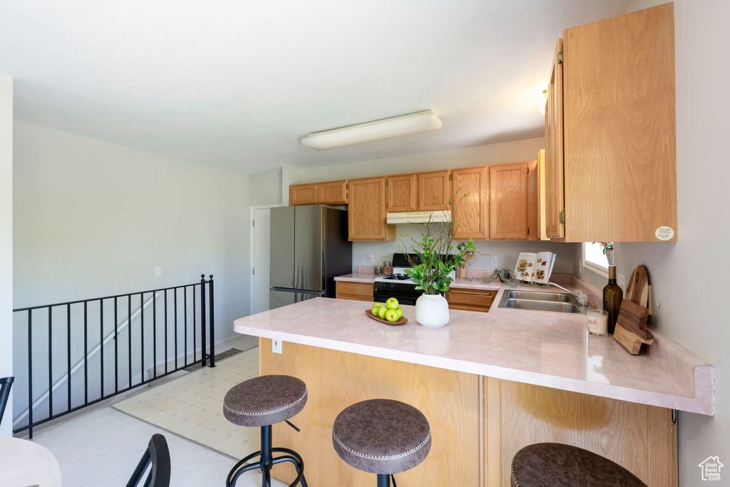 Kitchen with a sink, freestanding refrigerator, a peninsula, under cabinet range hood, and range with gas cooktop