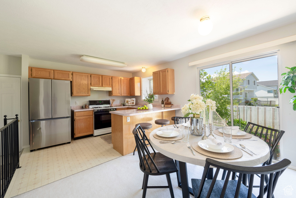 Kitchen with freestanding refrigerator, a peninsula, light colored carpet, light countertops, and gas stove