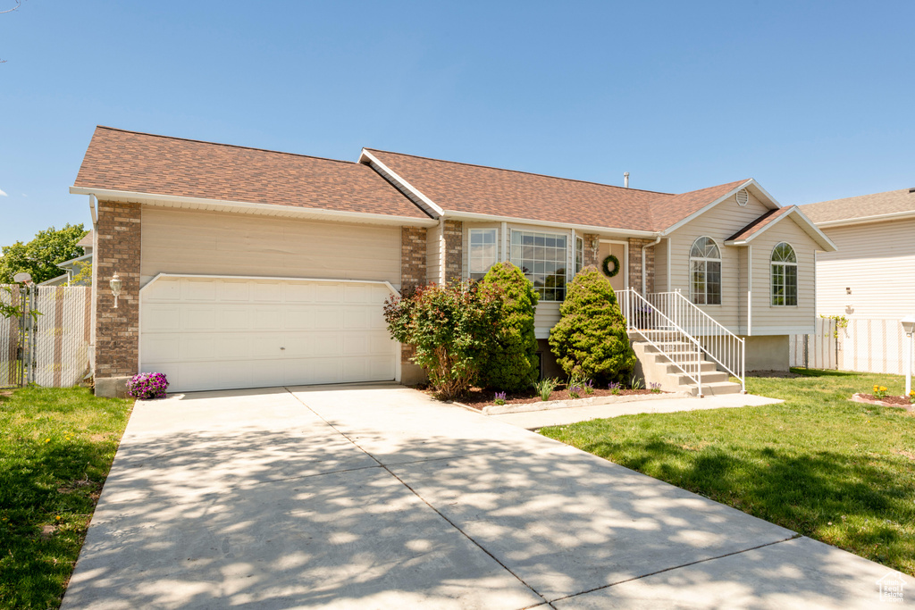 Ranch-style house featuring fence, roof with shingles, an attached garage, a front lawn, and driveway