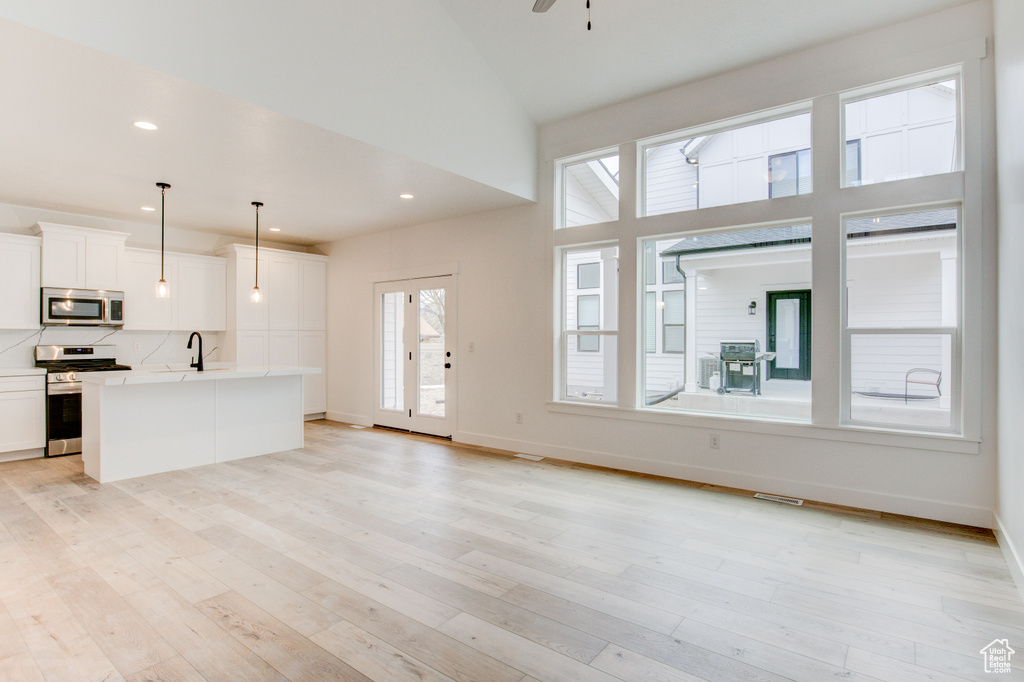 Unfurnished living room with a sink, high vaulted ceiling, light wood-style flooring, baseboards, and visible vents