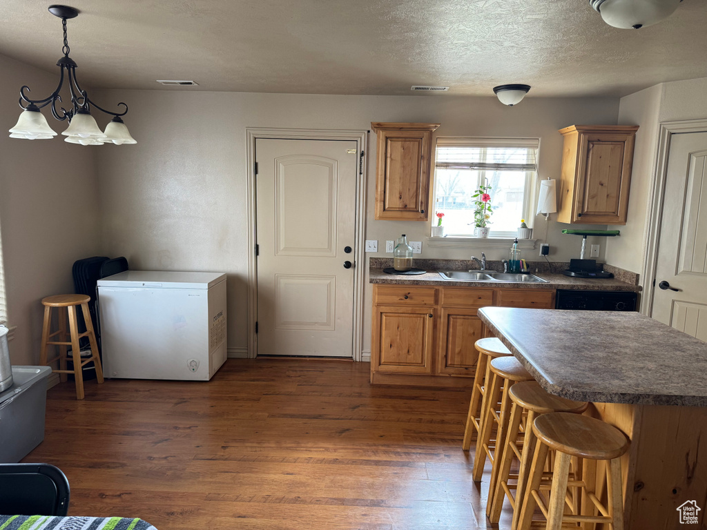 Kitchen with wood finished floors, dark countertops, a breakfast bar area, a sink, and white fridge