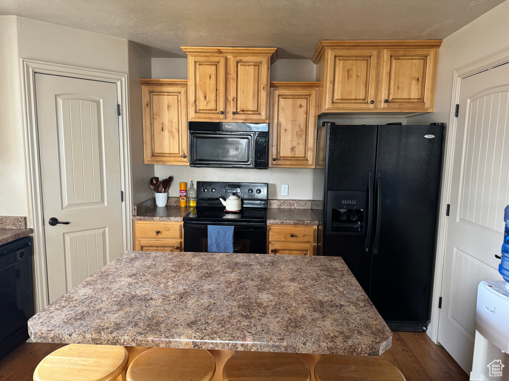 Kitchen featuring a breakfast bar area, dark wood finished floors, black appliances, and a center island