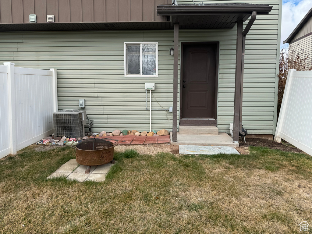 Doorway to property with fence, central air condition unit, and a lawn