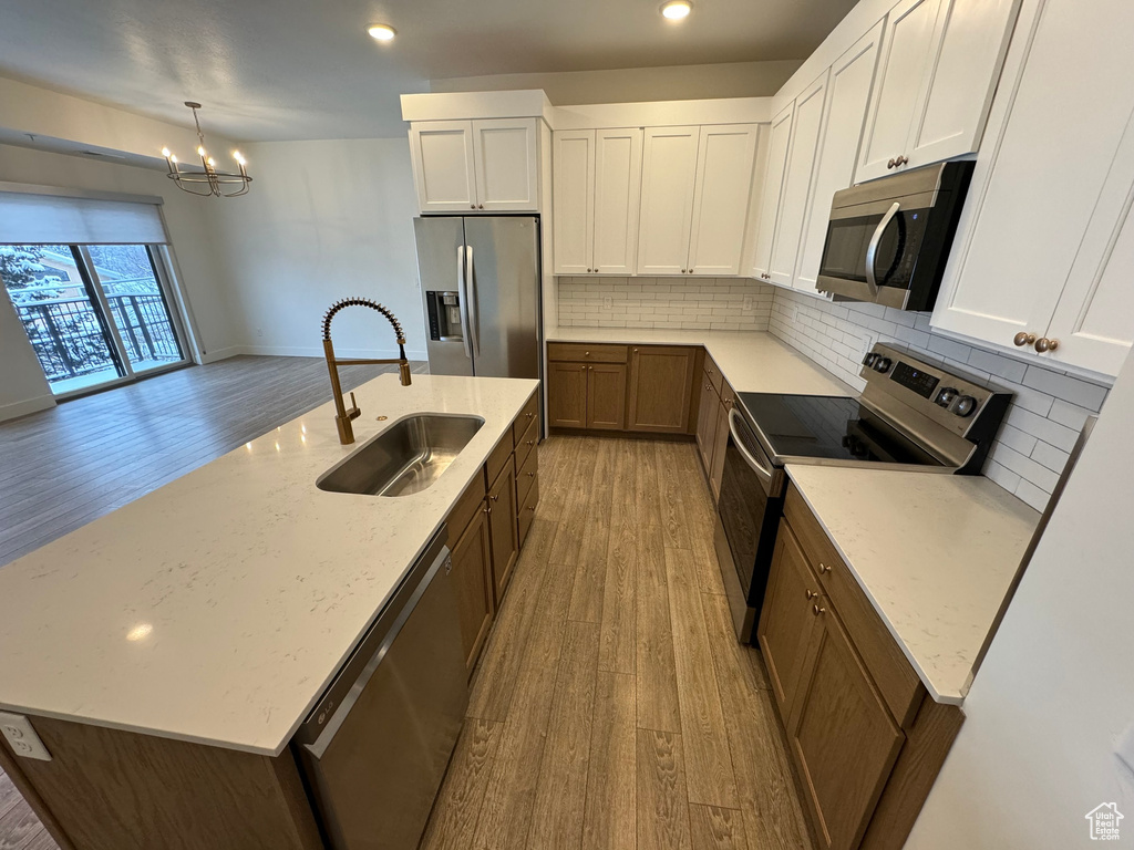 Kitchen featuring light wood-style floors, a center island with sink, a sink, backsplash, and stainless steel appliances