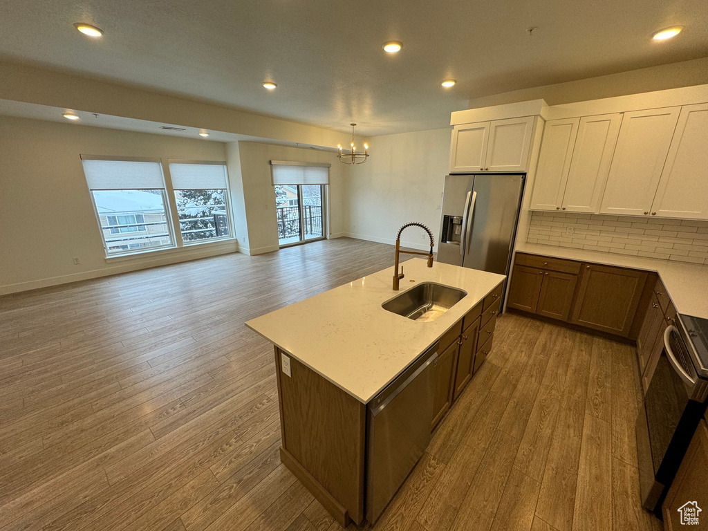 Kitchen with a chandelier, wood finished floors, a sink, open floor plan, and stainless steel fridge