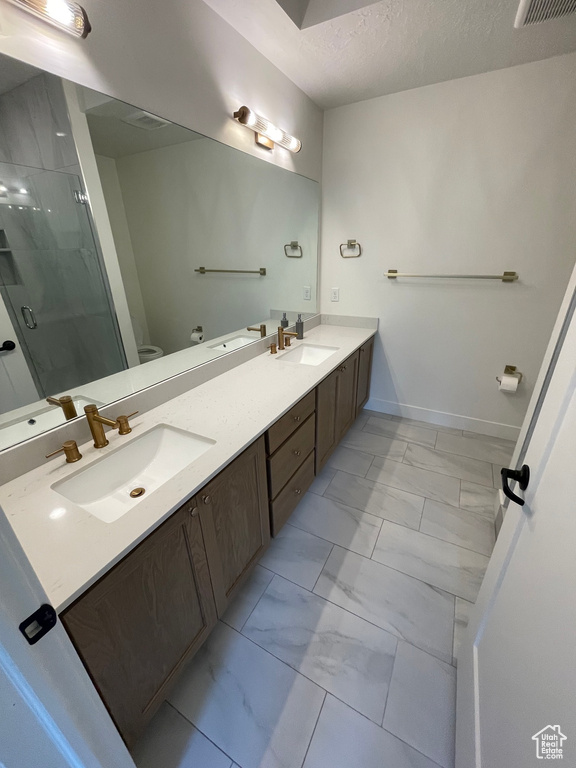 Bathroom with double vanity, a shower stall, a sink, toilet, and marble finish floor
