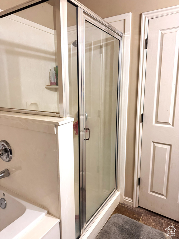 Full bath with baseboards, stone finish flooring, an enclosed shower, and a tub