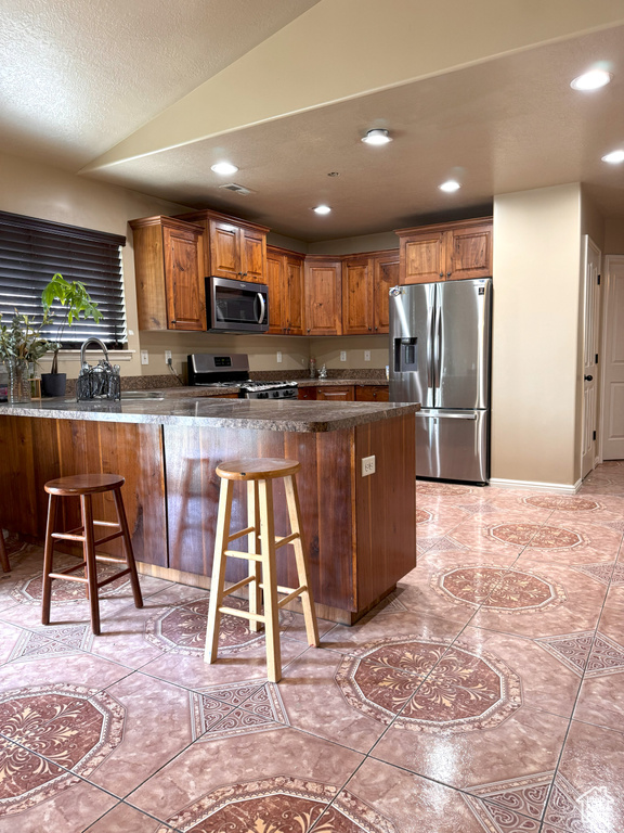 Kitchen featuring recessed lighting, appliances with stainless steel finishes, brown cabinetry, and a peninsula