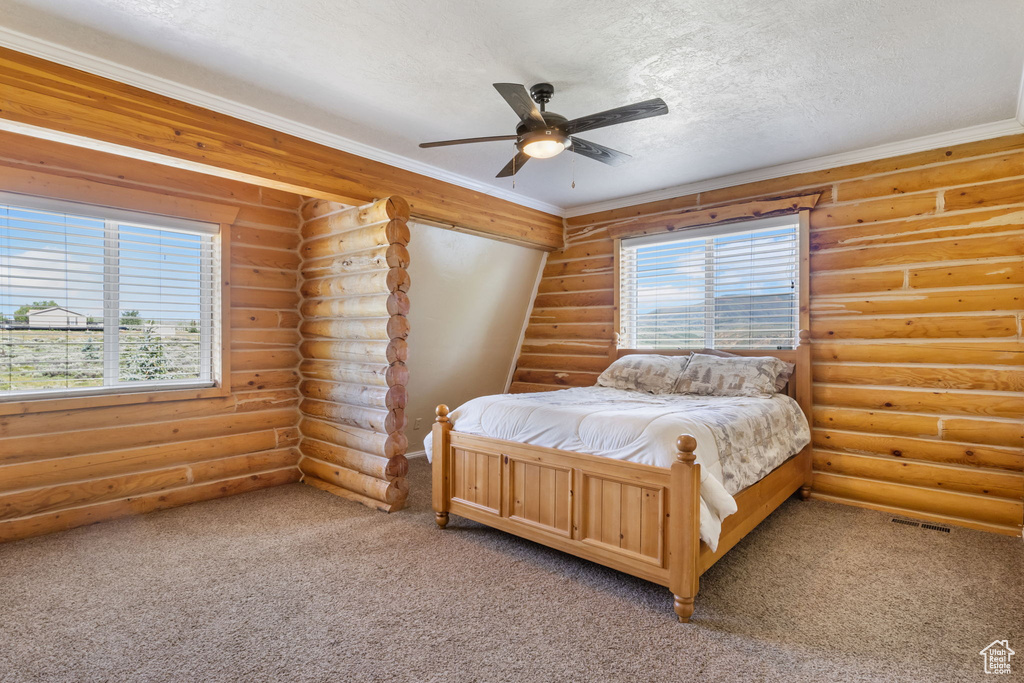 Bedroom with rustic walls, light colored carpet, and multiple windows