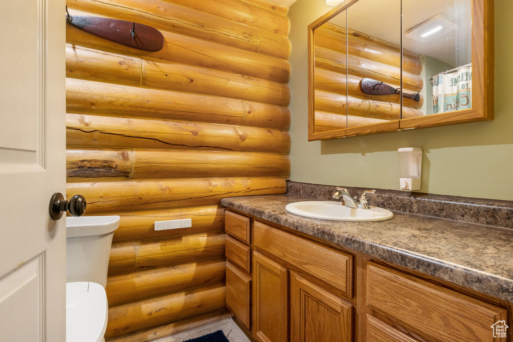 Full bath with log walls, vanity, and toilet