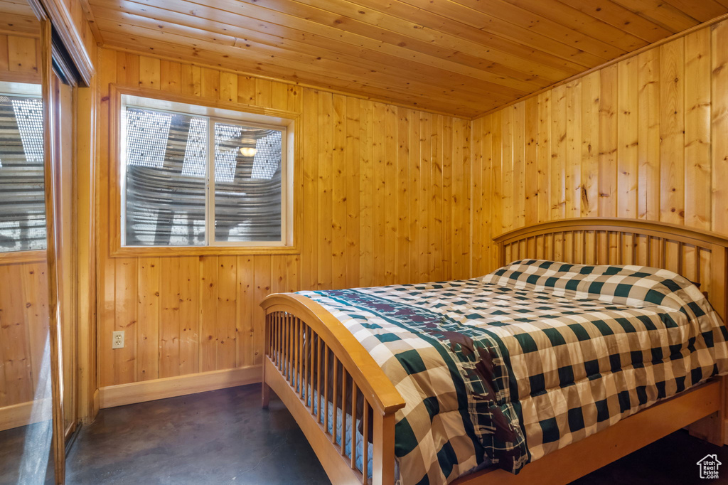 Bedroom with finished concrete floors, wood ceiling, wooden walls, and multiple windows
