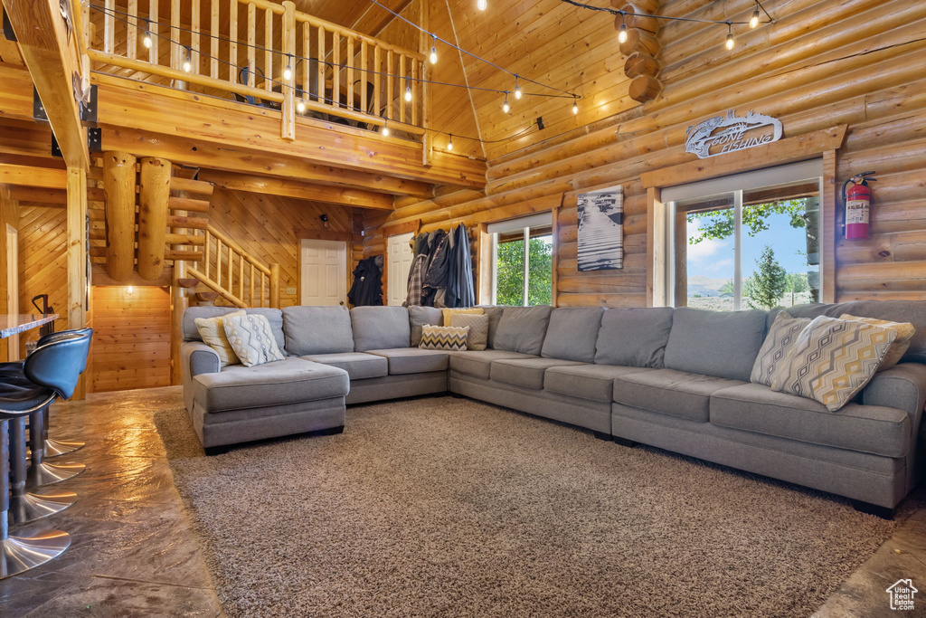 Living room with stairs, a towering ceiling, rustic walls, and wood ceiling