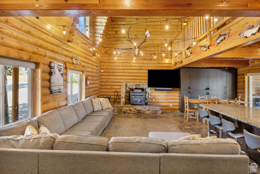Living room featuring wood ceiling, a towering ceiling, a wood stove, beamed ceiling, and rustic walls