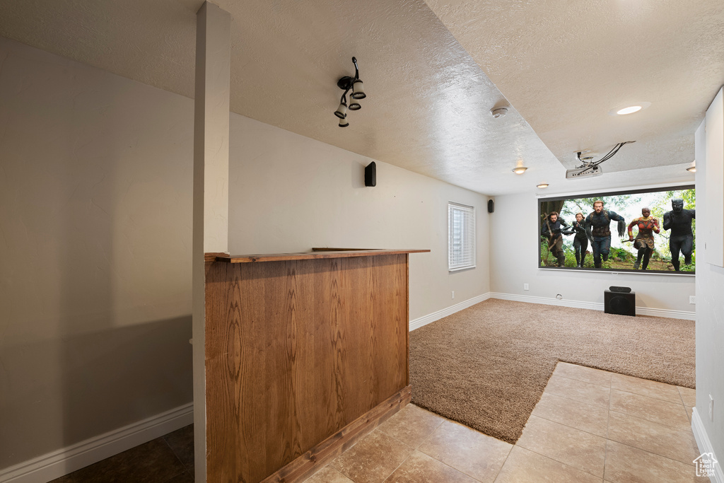 Home theater room featuring baseboards, a dry bar, a textured ceiling, and light carpet