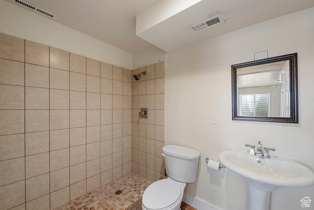 Full bath with visible vents, a tile shower, a sink, baseboards, and toilet