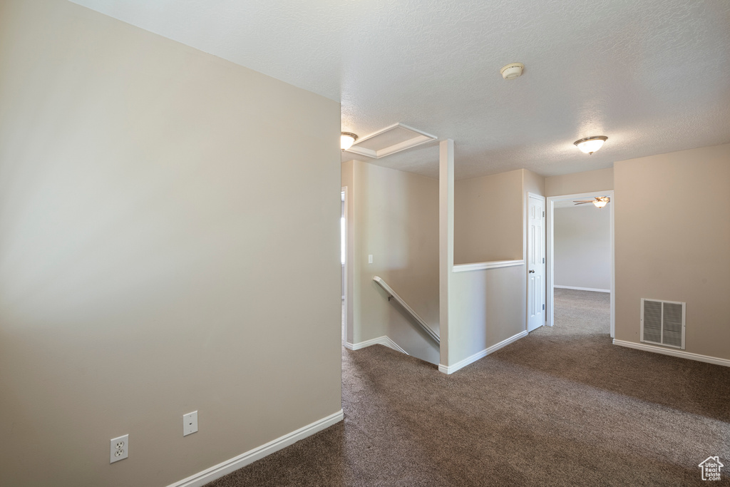 Empty room featuring attic access, a textured ceiling, visible vents, baseboards, and dark carpet