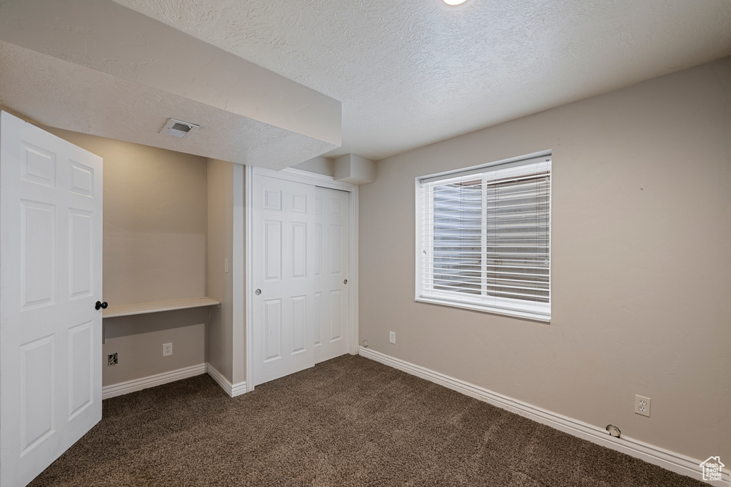 Unfurnished bedroom with baseboards, a textured ceiling, dark carpet, and a closet