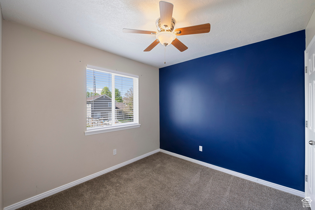 Carpeted empty room featuring baseboards, a ceiling fan, and a textured ceiling