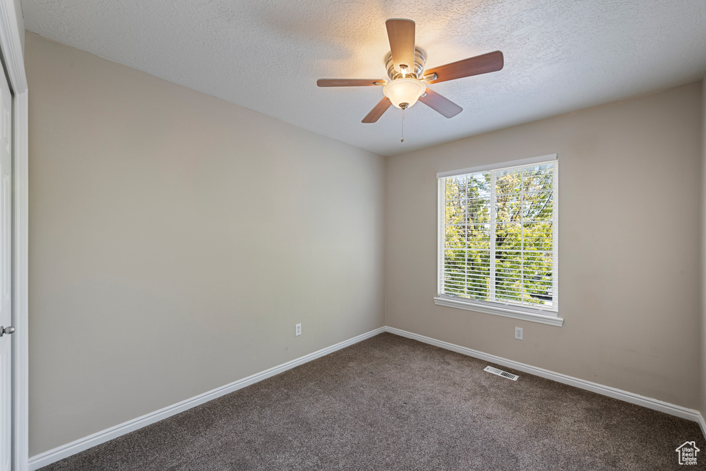 Carpeted spare room featuring baseboards, a textured ceiling, ceiling fan, and visible vents