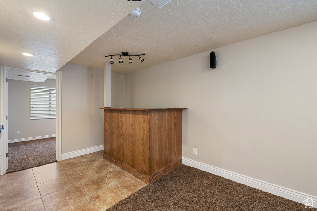 Bar with light carpet, a textured ceiling, baseboards, light tile patterned floors, and a bar